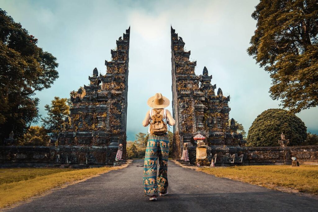 Reisende mit Rucksack und Strohhut vor dem Handara Gate, einem traditionellen Tempeltor auf Bali